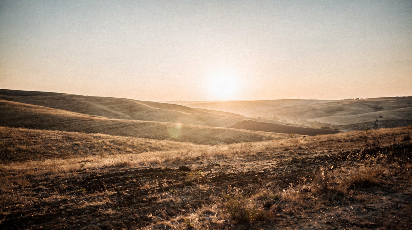 A wide dusk landscape of dry summer hills with the sun sitting very low and gold on the horizon