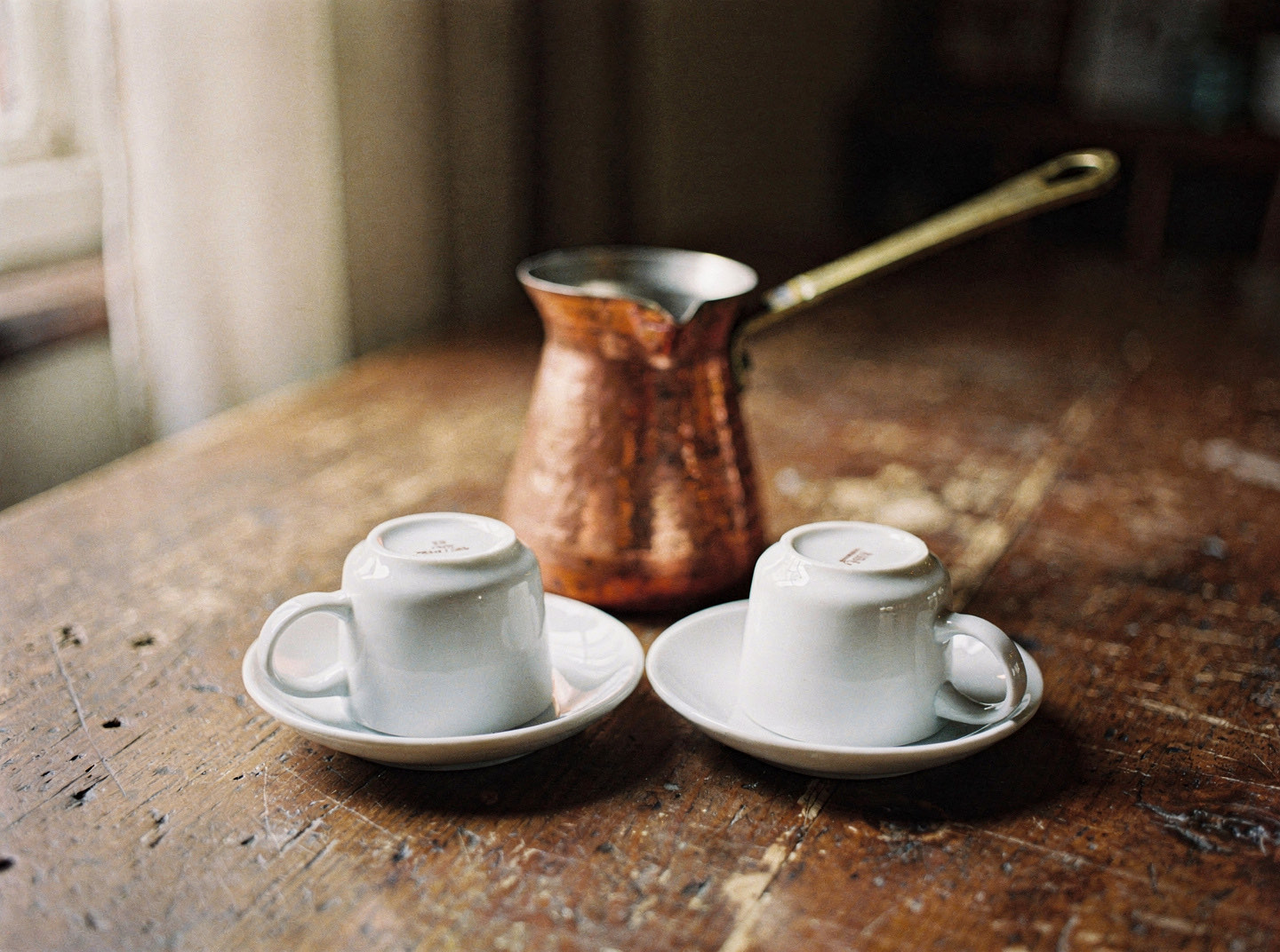 Two small cups upturned on their saucers on a wooden table beside a copper cezve